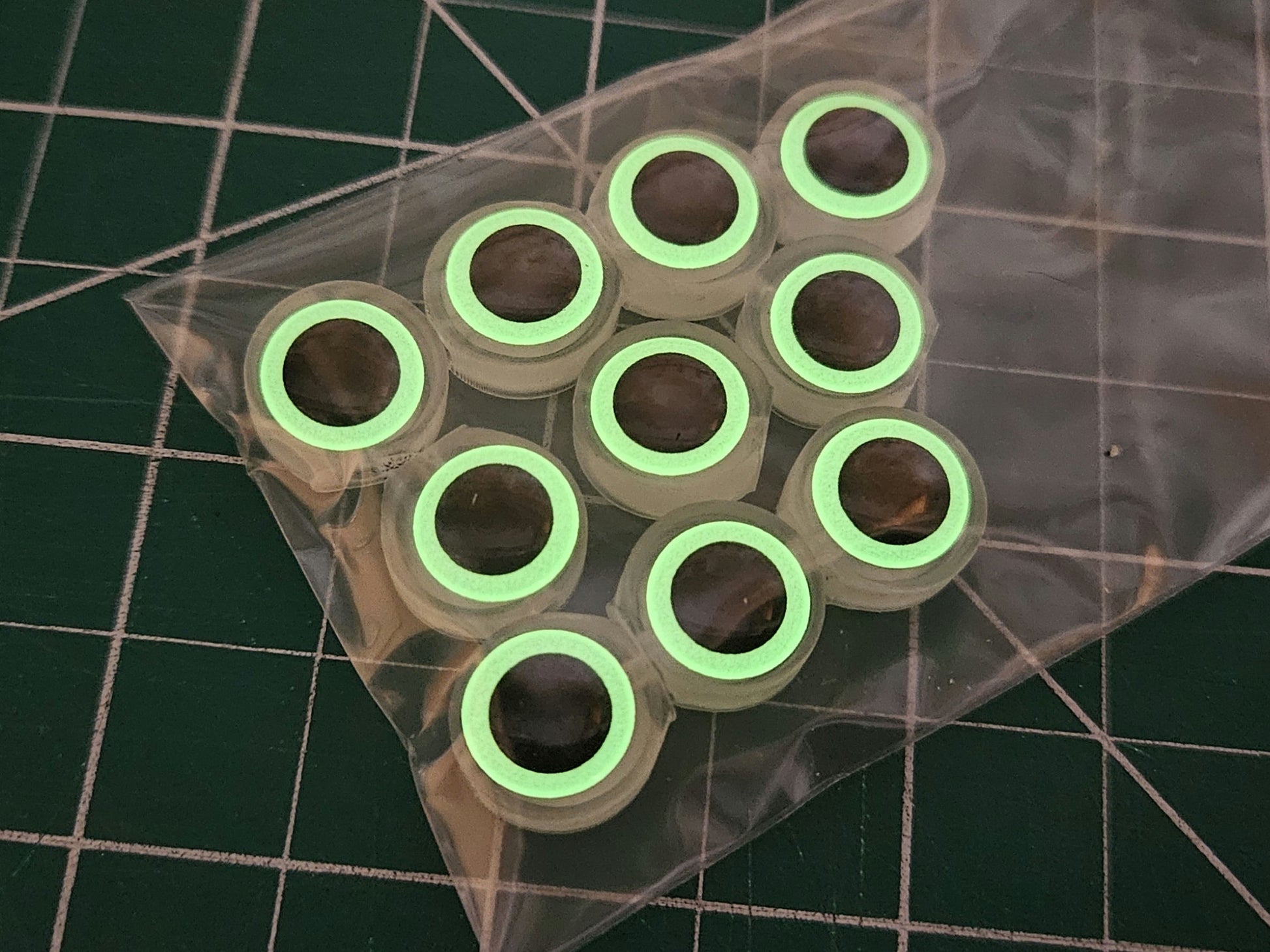 10-pack bag of BigEye Fishing Beads shown in dim light with eyes glowing strongly against green work mat.