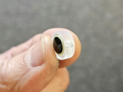 BigEye Trolling Fly BEAD close-up pinched between my fingers at an angle showing through hole, thickness of bead and eye background out of focus gray