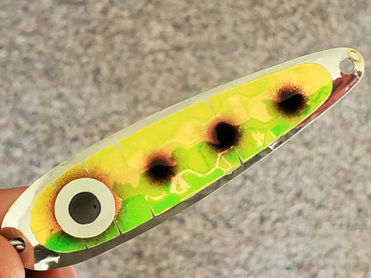 Fishing lure with green and yellow tape and black dots held by a hand on a neutral background