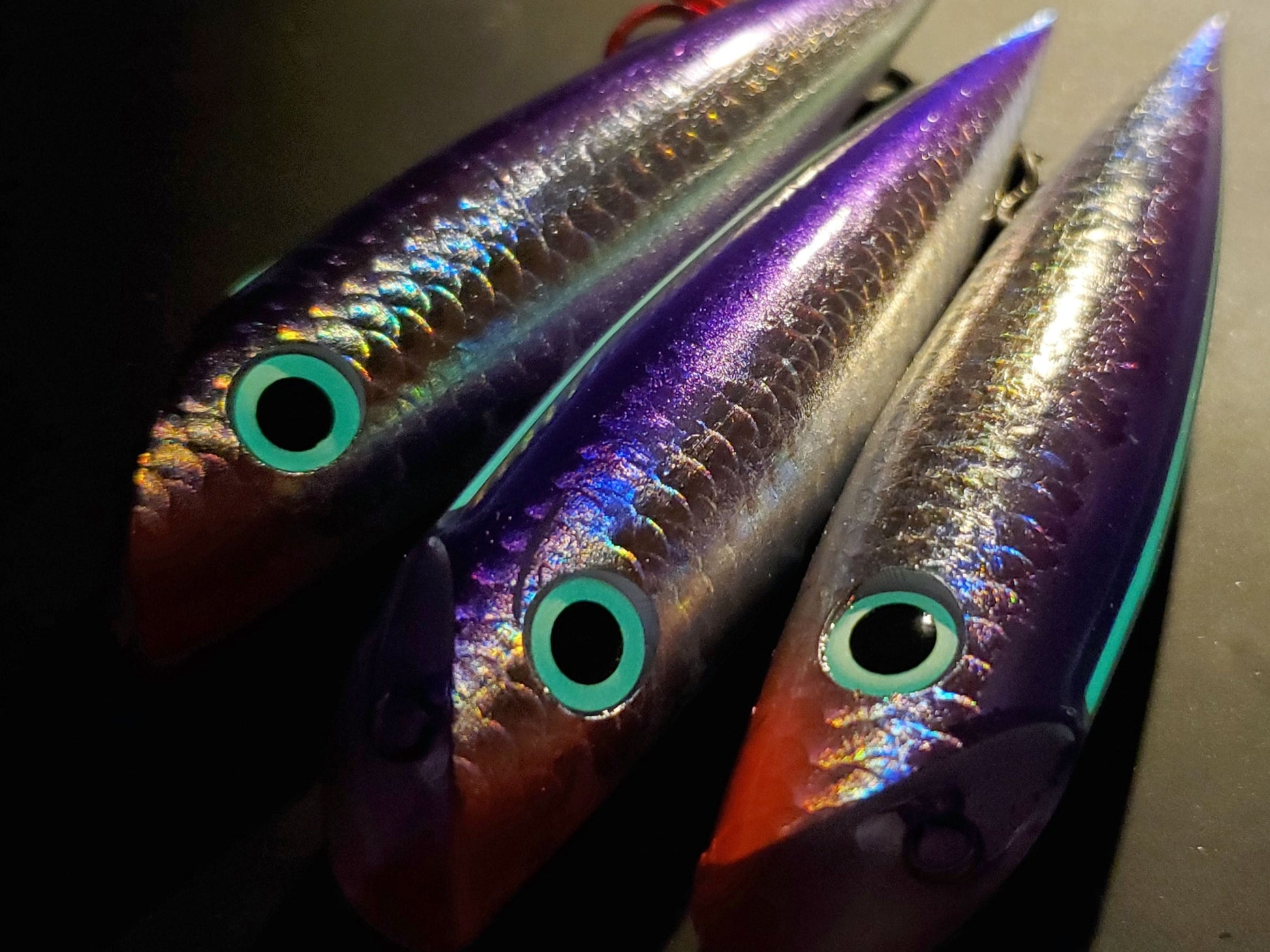 Three holographic trolling plugs with reflective surfaces and glowing eyes on a dark background.