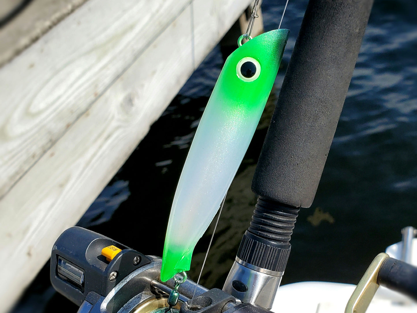 Green and white salmon plug attached to a fishing rod with water and boat deck in the background