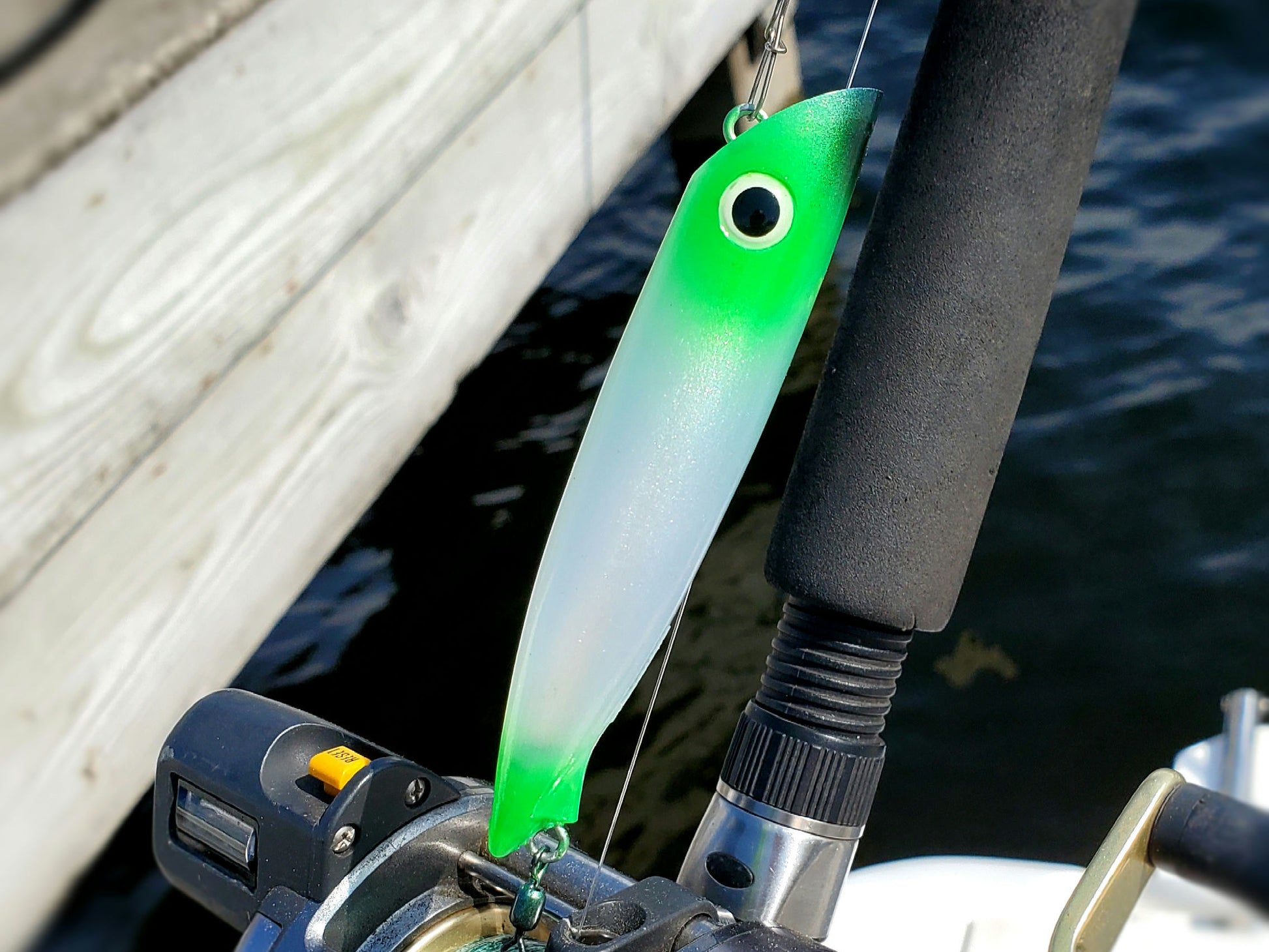 Green and white salmon plug attached to a fishing rod with water and boat deck in the background