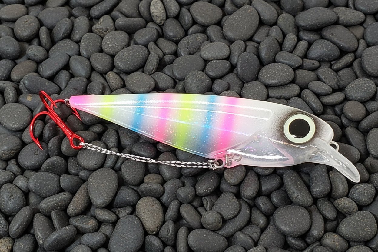 Salmon trolling lure FlatFin Minnow 'Tiger Bread' - Fisher Tackle Company laying on black gravel in daylight showing pink/blue/chartruese stripes over pearlescent undercoat