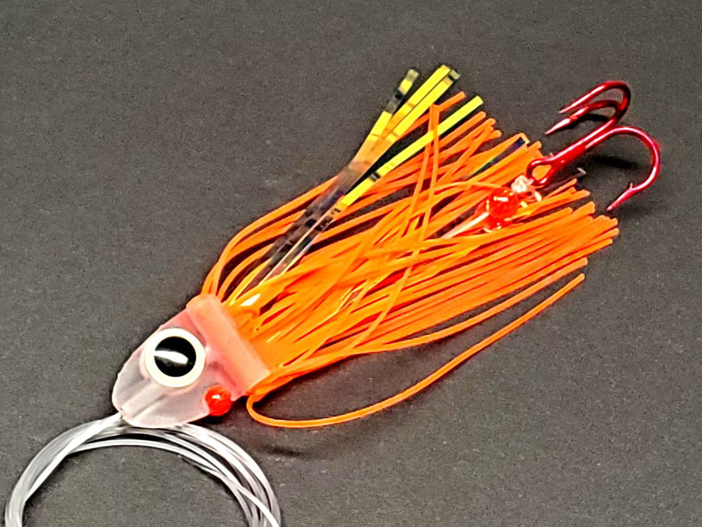 Salmon trolling fly with hot orange skirting and large glow eye on a gray background