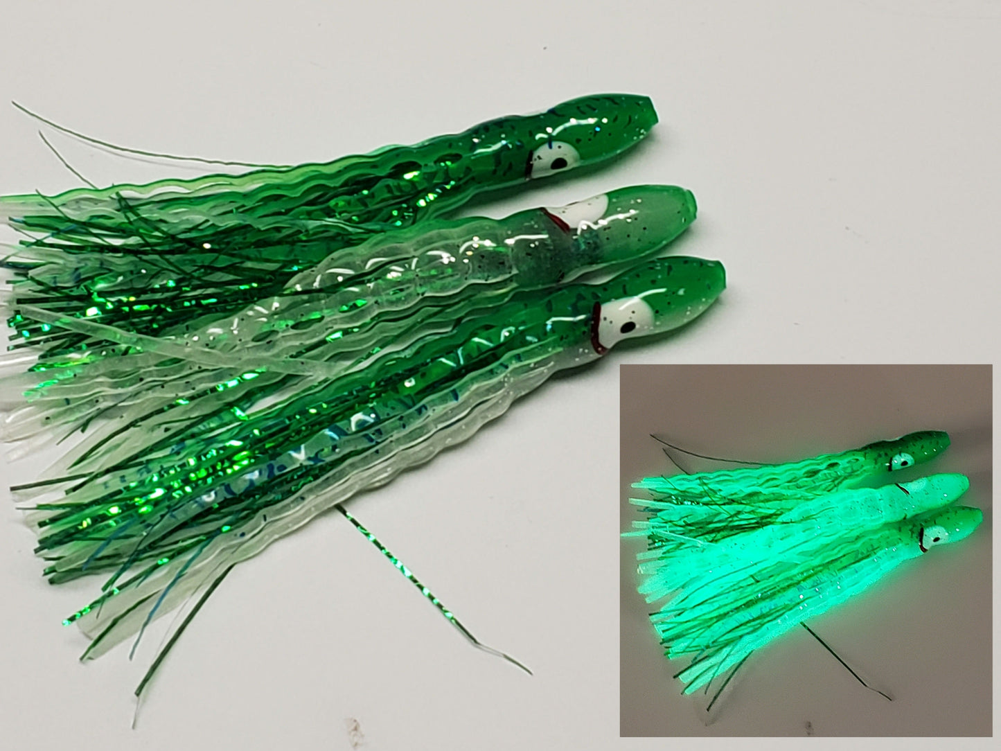 3 Green glow with green sparkle backs salmon Hoochie Squids with dark green holographic Mylar Inserts laying on white background...inset glowing in dark