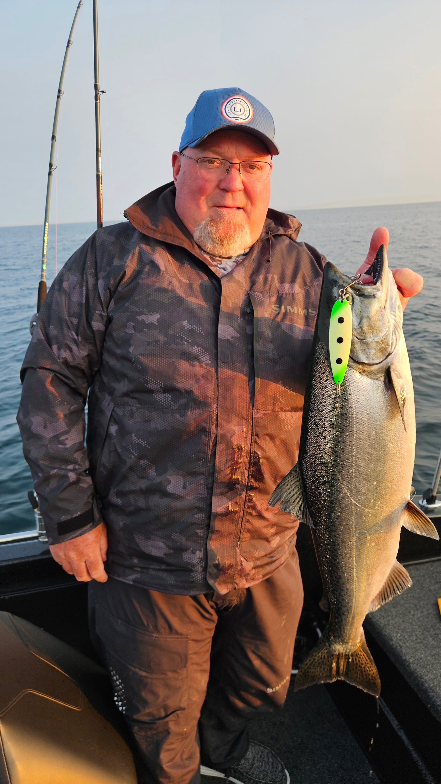 Man holding a large king salmonwith a green and black glow spoon hanging from mouth in boat