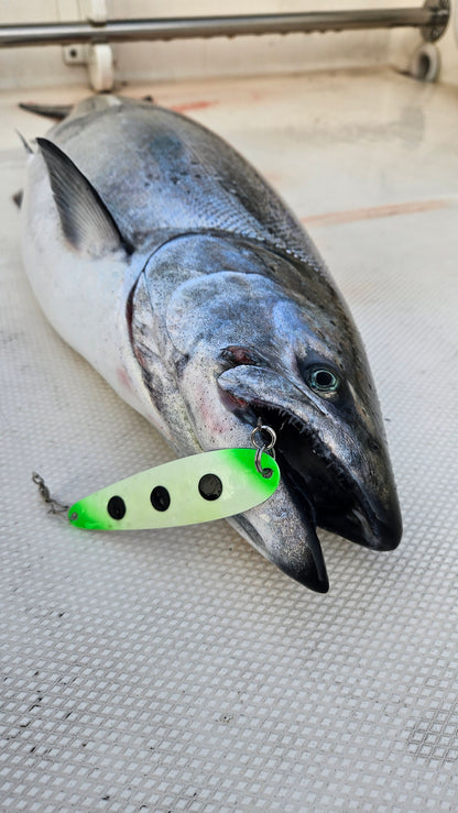 Green glow spoon with black dots in the mouth of a salmon on a white boat deck