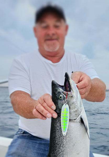 Man holding a salmon with a green and white spoon hanging from mouth out in boat over water