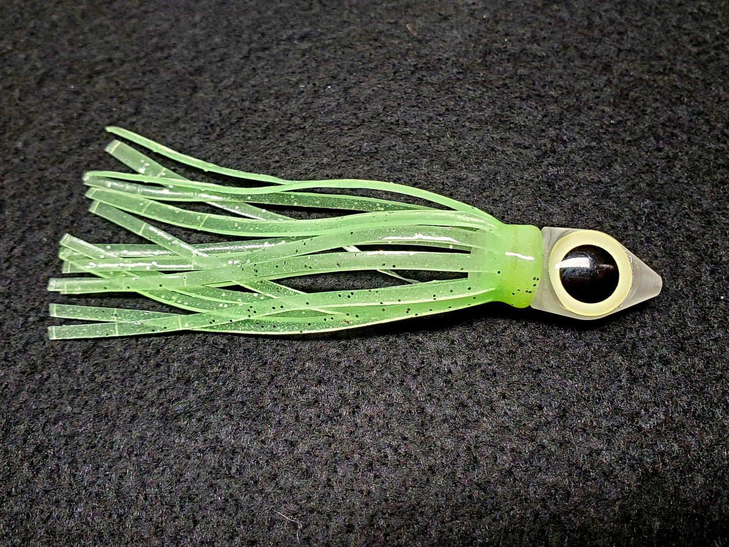 Green squid fishing lure with a black eye on a dark background
