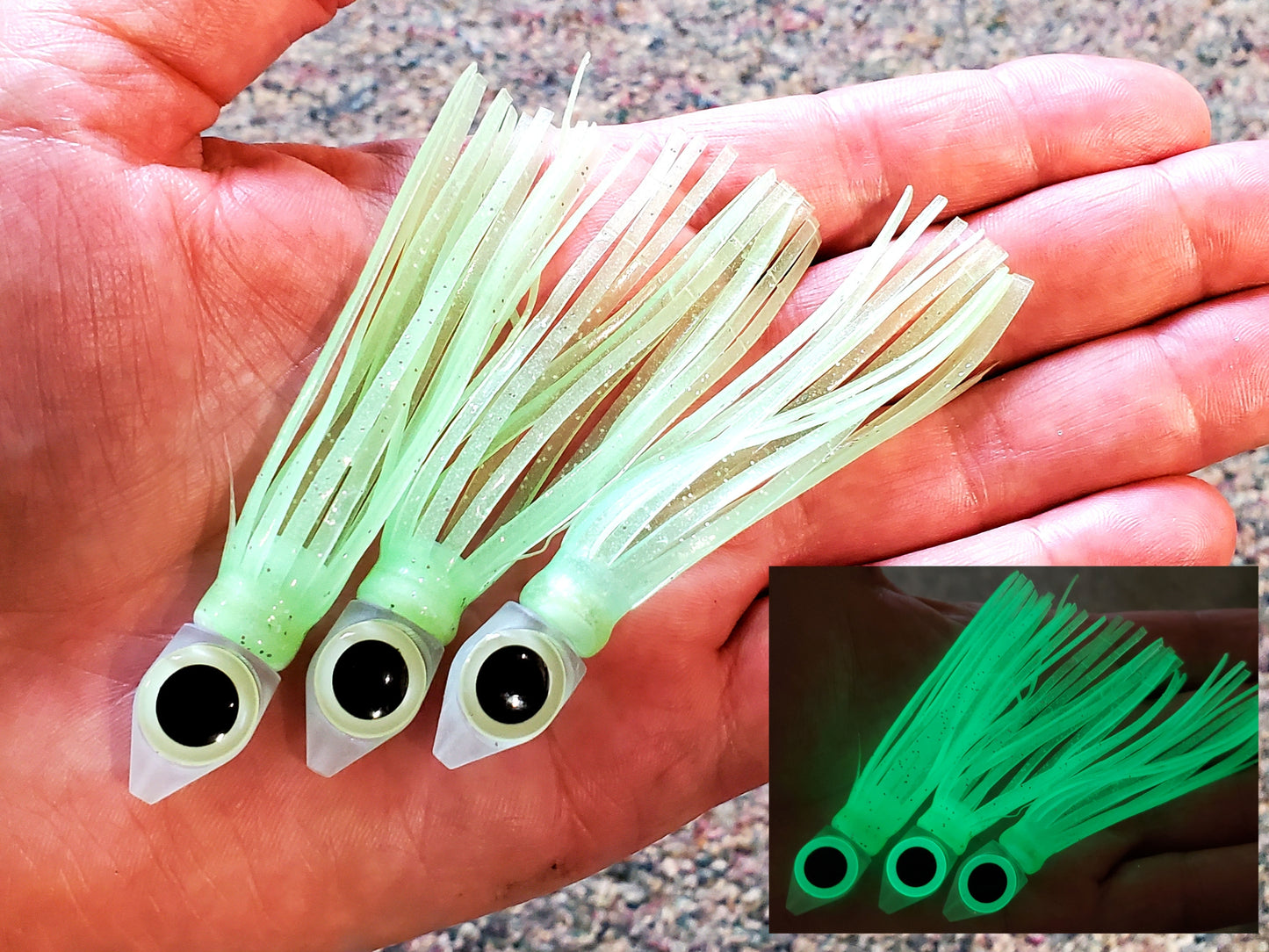 Pale Green squid-type lures with black eyes held in a hand.  Inset shows them glowing in dark.