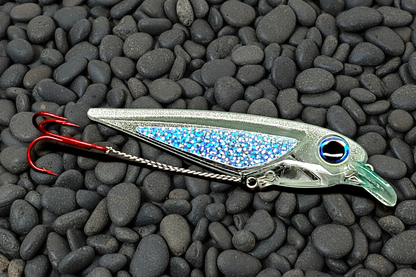FlatFin FlashBang silver glitter and light pale blue trolling lure laying on dark gray pebble background