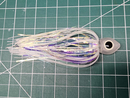 Side view of a Floating Squid Fly with a milky translucent hollow head, large black and glow eyes, and iridescent white and glow silicone skirting on a green mat.