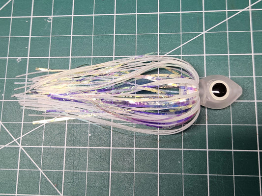 Side view of a Floating Squid Fly with a milky translucent hollow head, large black and glow eyes, and iridescent white and glow silicone skirting on a green mat.