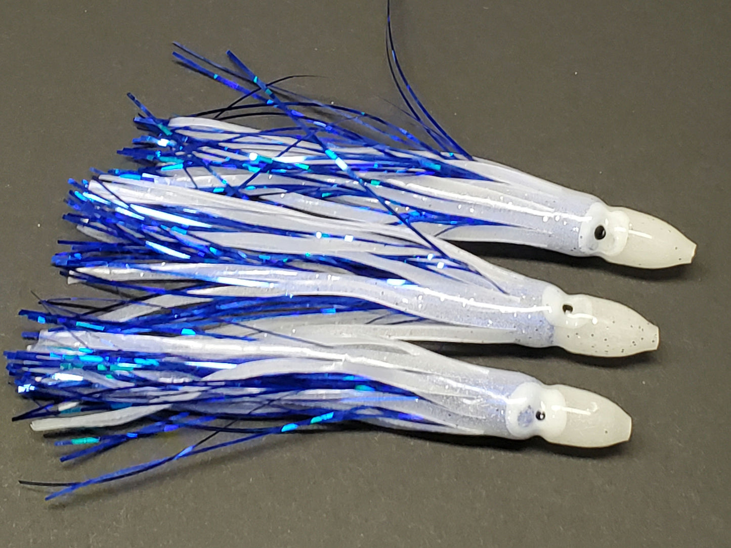 Three Glow/Blue 4.5-inch hoochie squids with blue crinkle Mylar inserts and white/black eyes, shown on a dark background