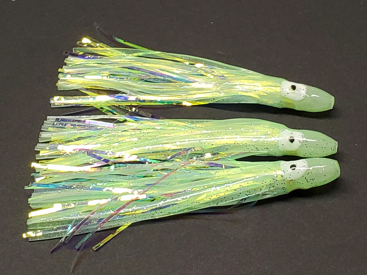 3 Pale green Glow Hoochie Squids with pearl holographic Mylar Inserts laying on dark background